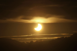 image of a sunrise with the sun partially eclipsed between clouds.